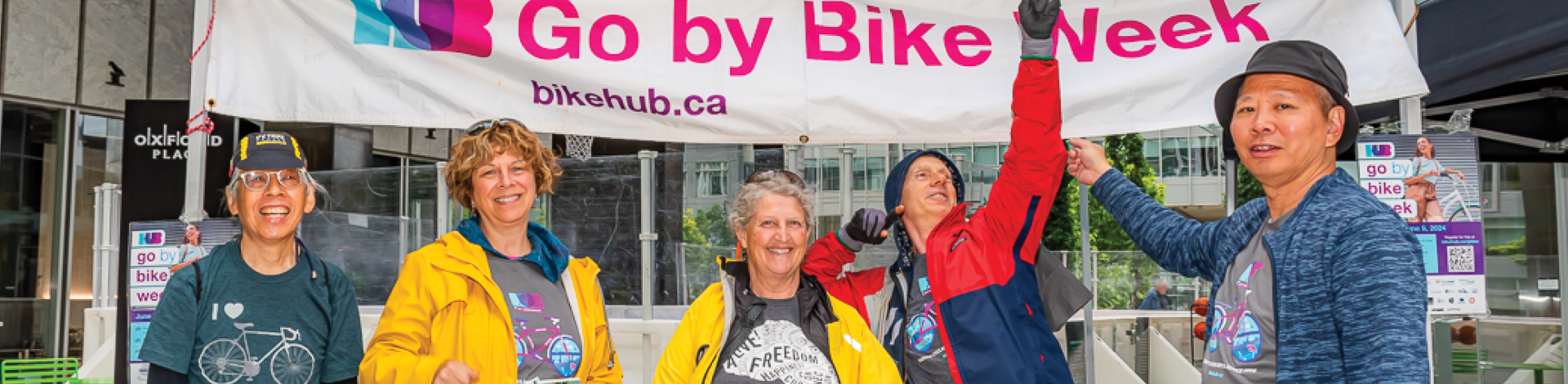 Five volunteers smile for the camera as they strike poses under a 'Go by Bike Week' tent.