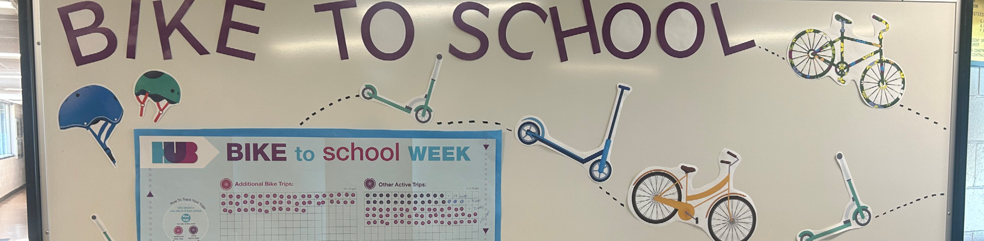 A whiteboard that reads: "BIKE TO SCHOOL" with various cut stickers of bikes, helmets, and scooters. The white board also has the Bike to School Week trip tracking poster taped to it.