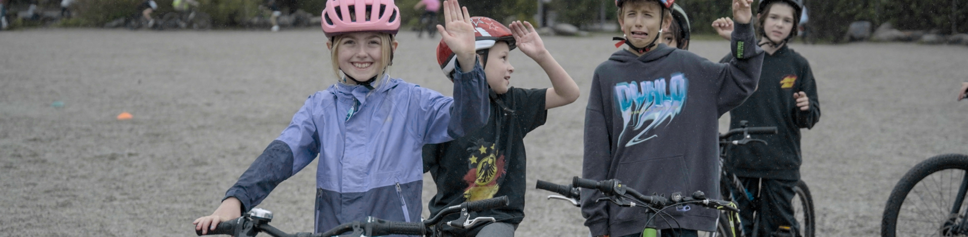 Five students indicate a right hand turn single with their right arm bent at the elbow. They are all wearing helmets and on bikes. One boy is making a silly crying face.