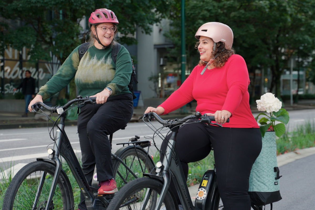 Two women ride e-bikes on a bike path.