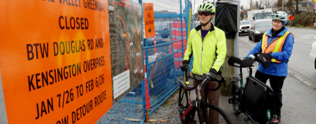 Two cyclists stand with their bikes as they read detour signage.