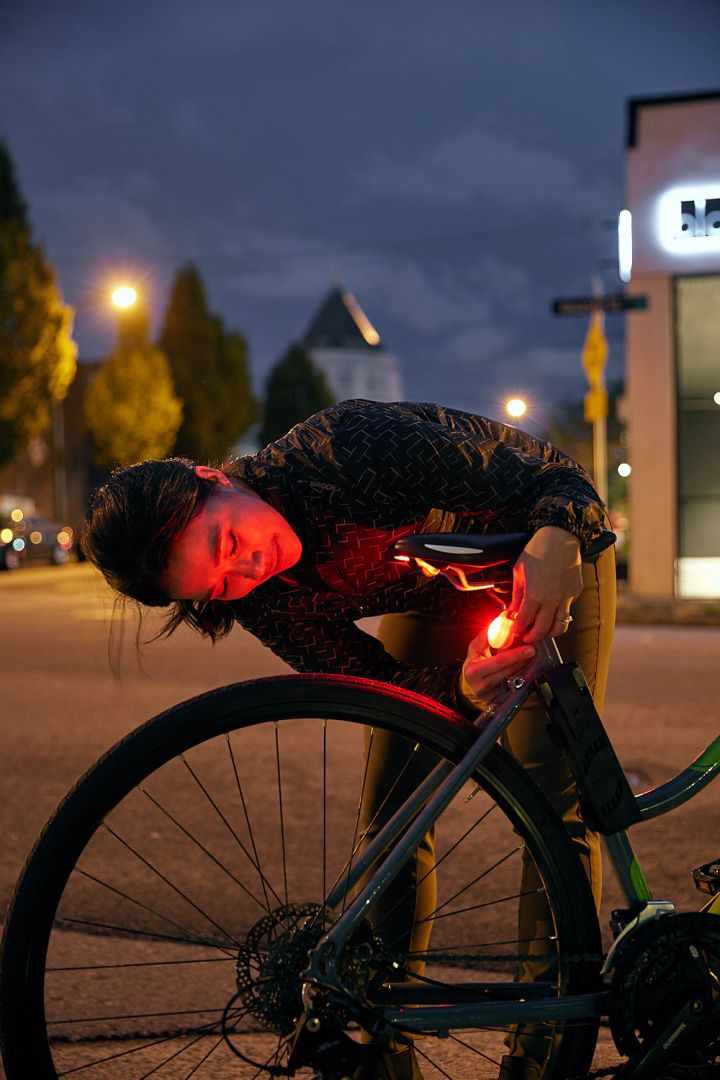 A woman fastens a red rear light to the back of her bike. It is night.
