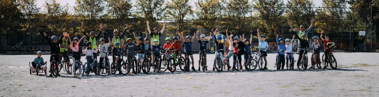 A group of students, teachers, and instructors pose for a group photo with bikes on school grounds.