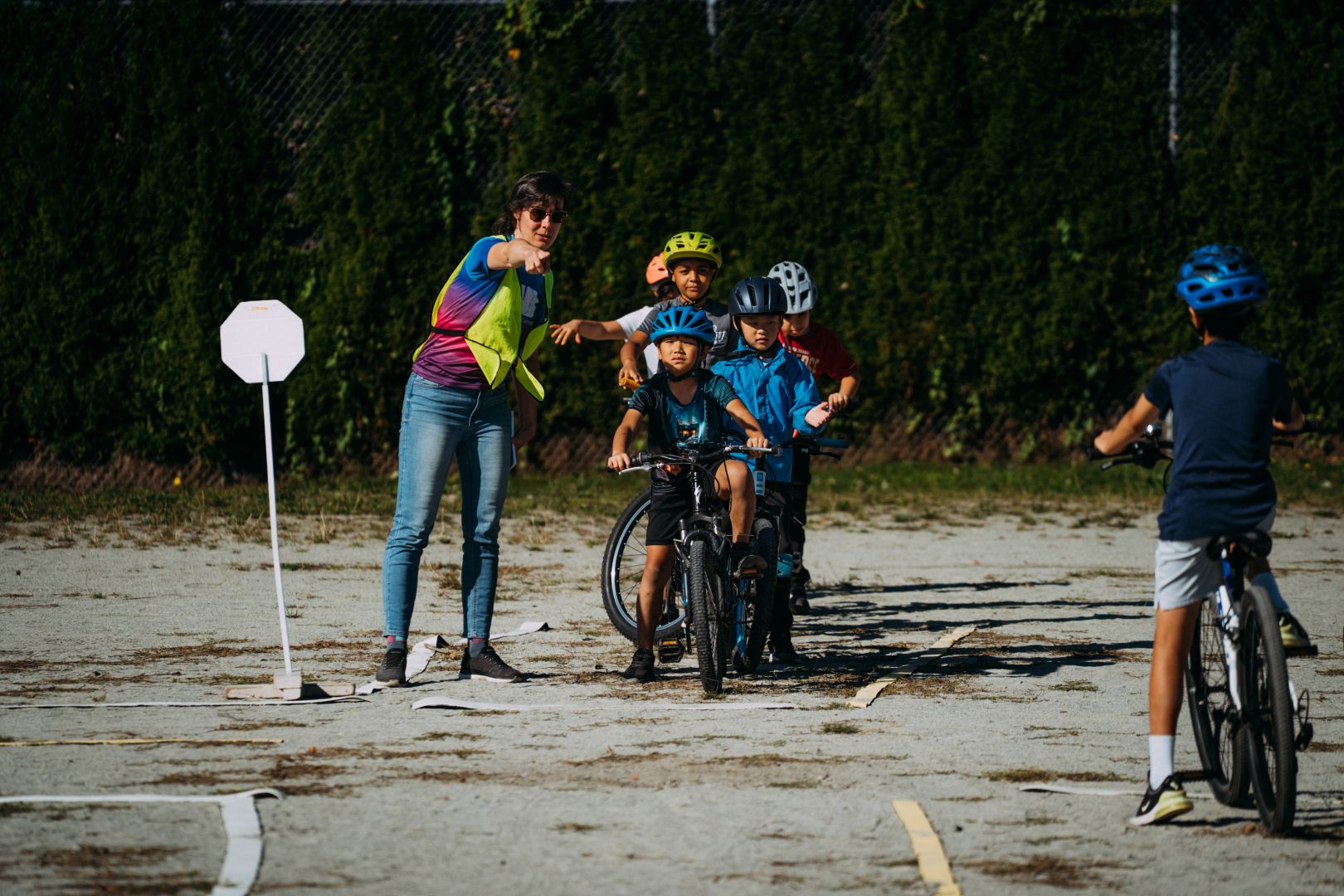 An instructor points at something in the distance as she speaks to students on their bikes.