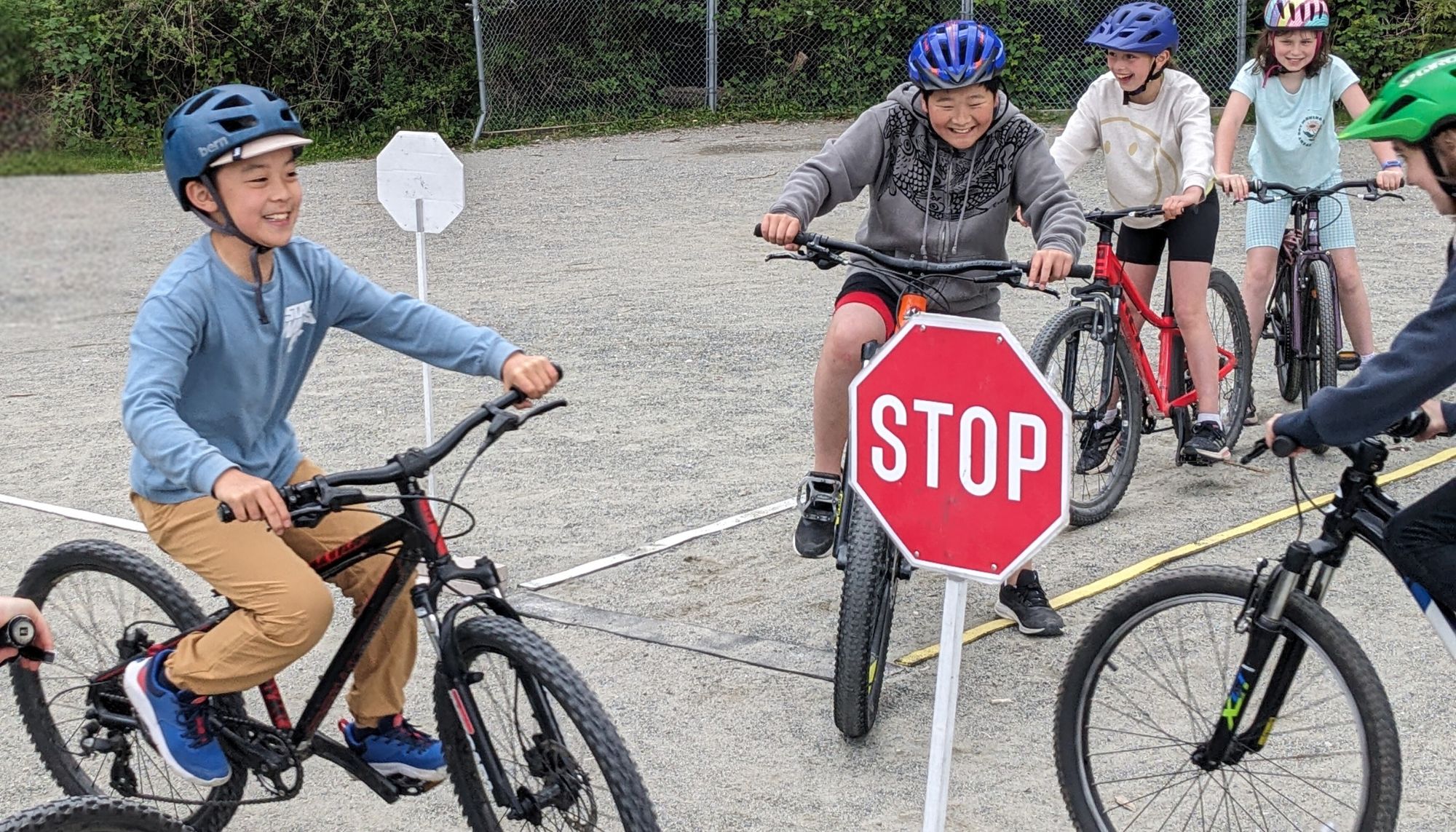 A group of school-aged children ride bikes in a two-way stop scenario.
