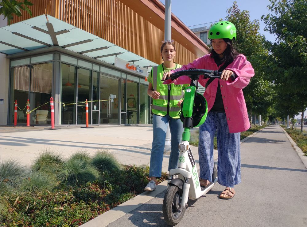 A woman begins to ride an e-scooter while an instructor observes.