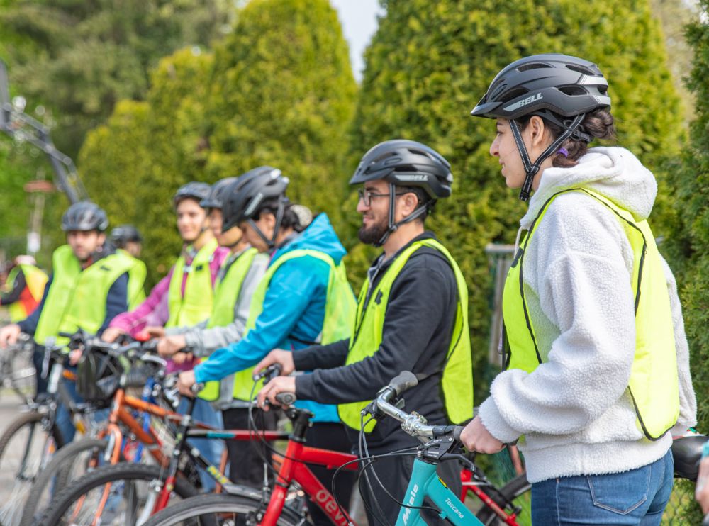 A group of adult stand with their bikes listening to the instructor.