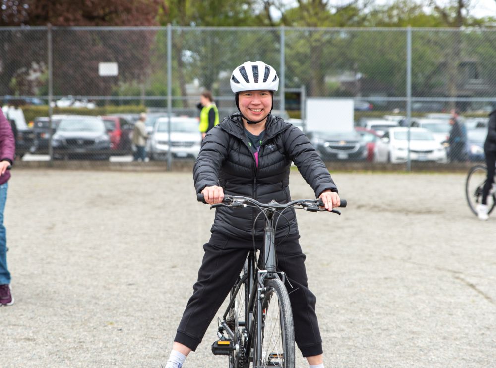 A woman rides their bike on a gravel field.