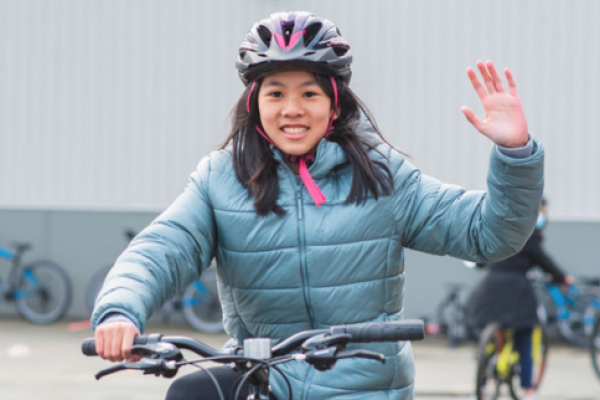 A girl rides her bike and indicates a right-turn signal with her arm.