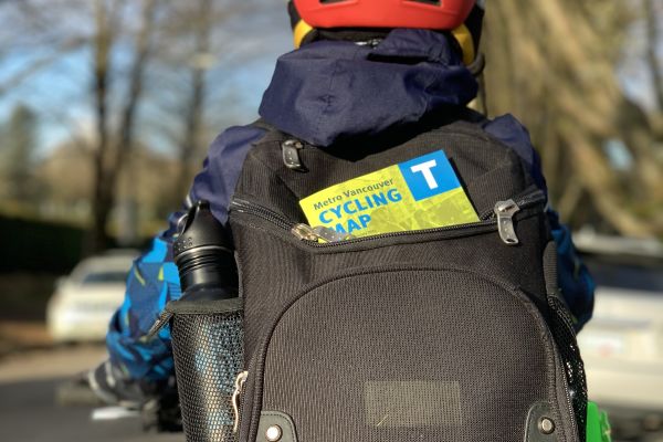 A boy rides his bike with a bike map sticking out of his backpack.