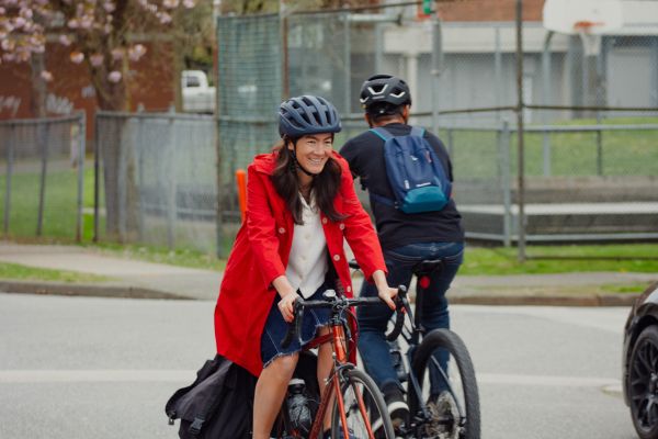 A woman in a red jacket rides a bike on a road. A man is riding a bike in the opposite direction.
