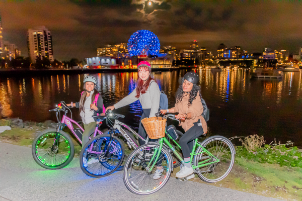 Three women with their bikes on the Seawall at night.