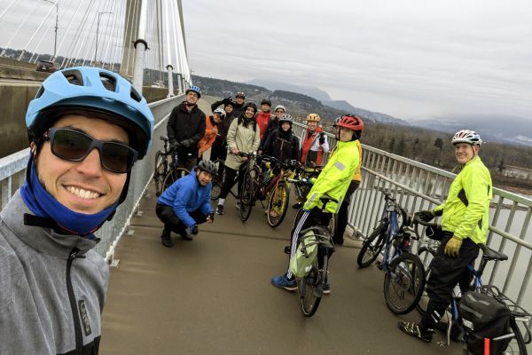 A group of people pose for a photo with their bikes on a bridge.