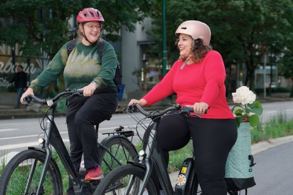Two women ride bikes on a bike path. They are smiling and laughing.