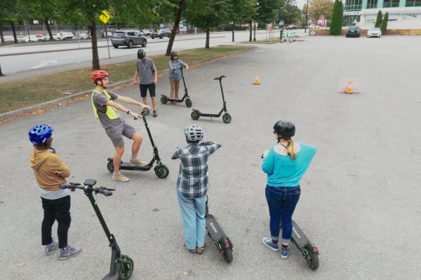 A group of people with e-scooters on a gravel field.