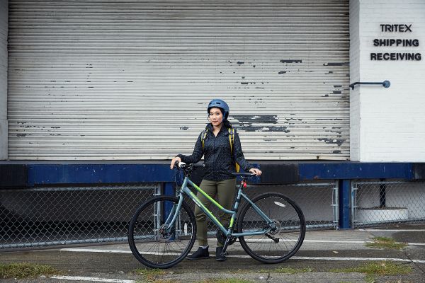 A woman stands with her bike in front of an industrial garage door.