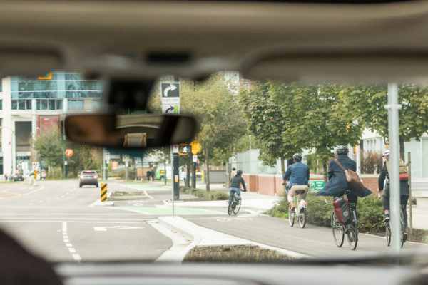 A person looks in their rearview mirror as they drive their vehicle. The road in front of them is seen through the windshield.