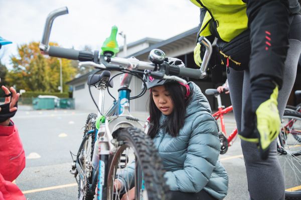 A girl performs bike maintenance on her bike on school grounds.