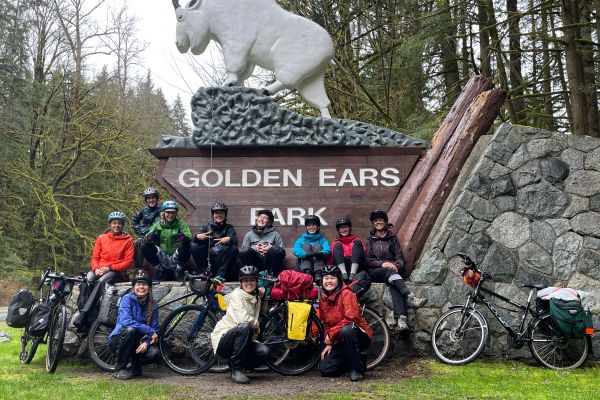 A group of women pose with their bikes in front of the 'Golden Ears Park' sign.