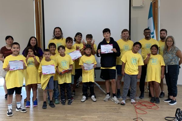 Students, instructors, and teachers pose for a photo in a classroom. Several students are holding up certificates of completion.
