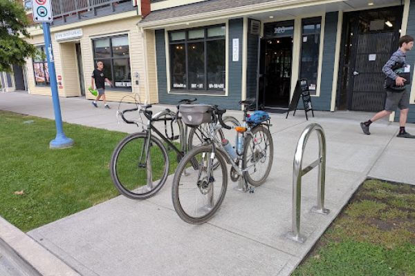 Two bikes parked at a bike rack in front of a store front.