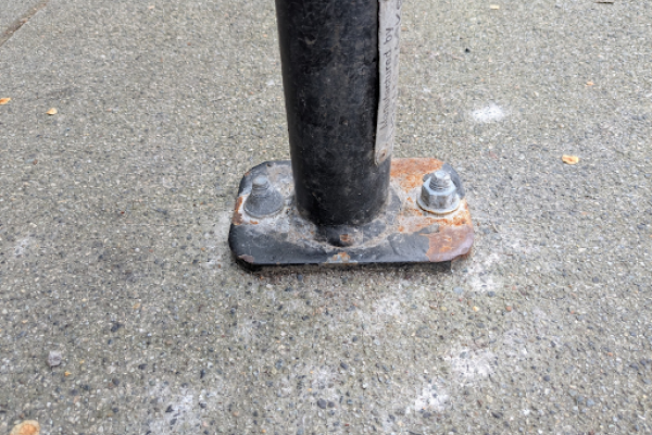 The bottom of a bike rack. Two fasteners can be seen, fastening the rack to the cement ground.