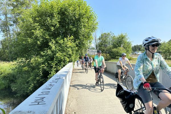 A group of people ride their bikes on a cycling path in Metro Vancouver. The weather is beautiful with blue skies.