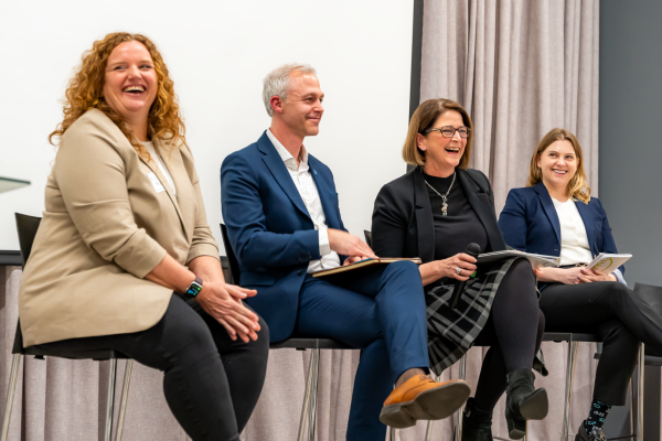 Four people laugh together as they sit on a panel.