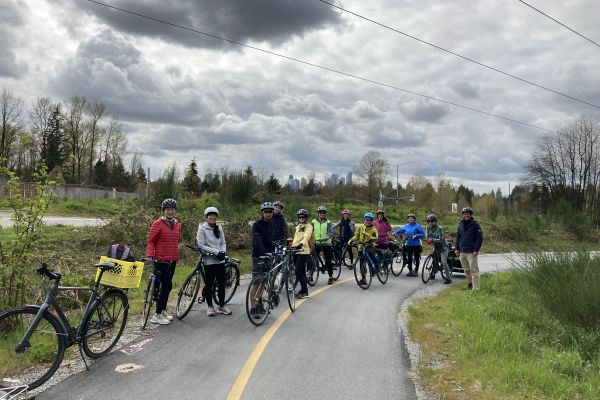 group of people standing next to their bikes on a quiet road surrounded by field with gray clouds