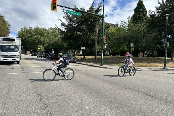 children crossing street with bike at intersection with truck waiting at red light