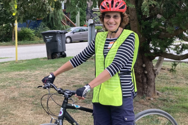 Roberta Walker, a woman in her 60s, stands with her bike. She is wearing a yellow vest and a red helmet.