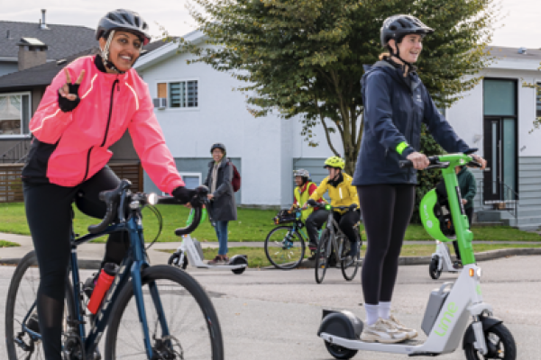1 person on bike smiling and one person on scooter smiling riding down a neighborhood street