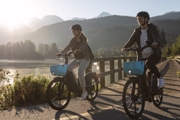 Two young adults ride BCAA's Evolve e-bikes on a multi-use paved trail in Whistler.