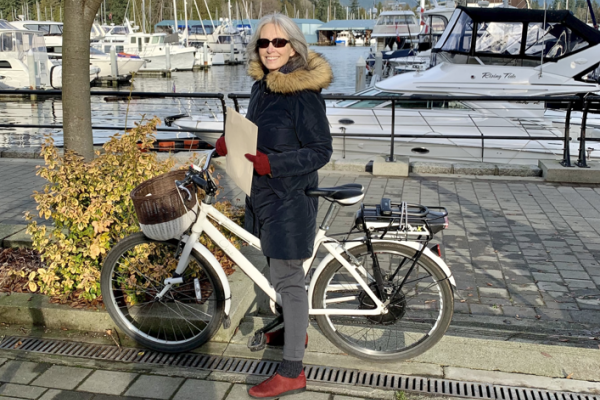 A photo of Dr. Kay Teschke and her bike on the Seawall. We can see the harbor with various boats parked behind her.