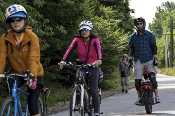 Several people ride bikes and other micromobility devices on a multi-use path.