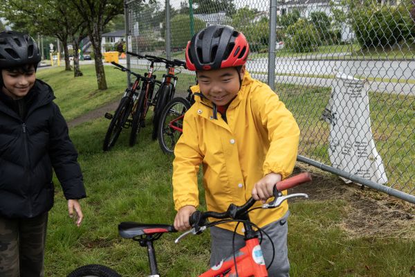 A young boy wearing a yellow winter jacket holds his bike's handle bars and smiles. Another boy wearing a black jacket smiles beside him.
