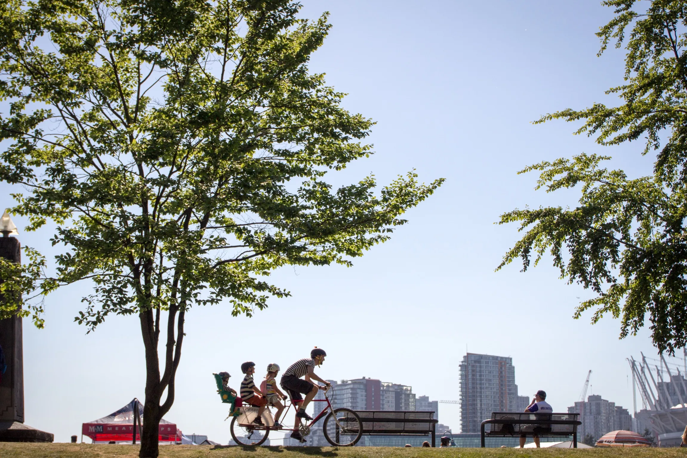 A father rides a bike with three children on the back.