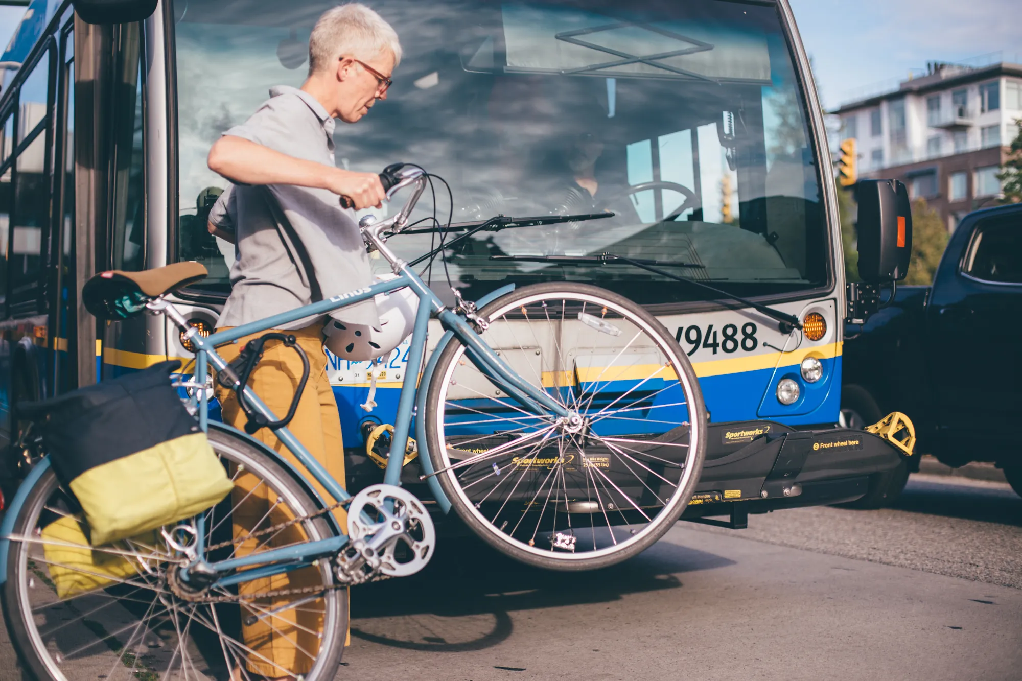 A woman lifts her bike onto the front of a TransLink bike bus rack.
