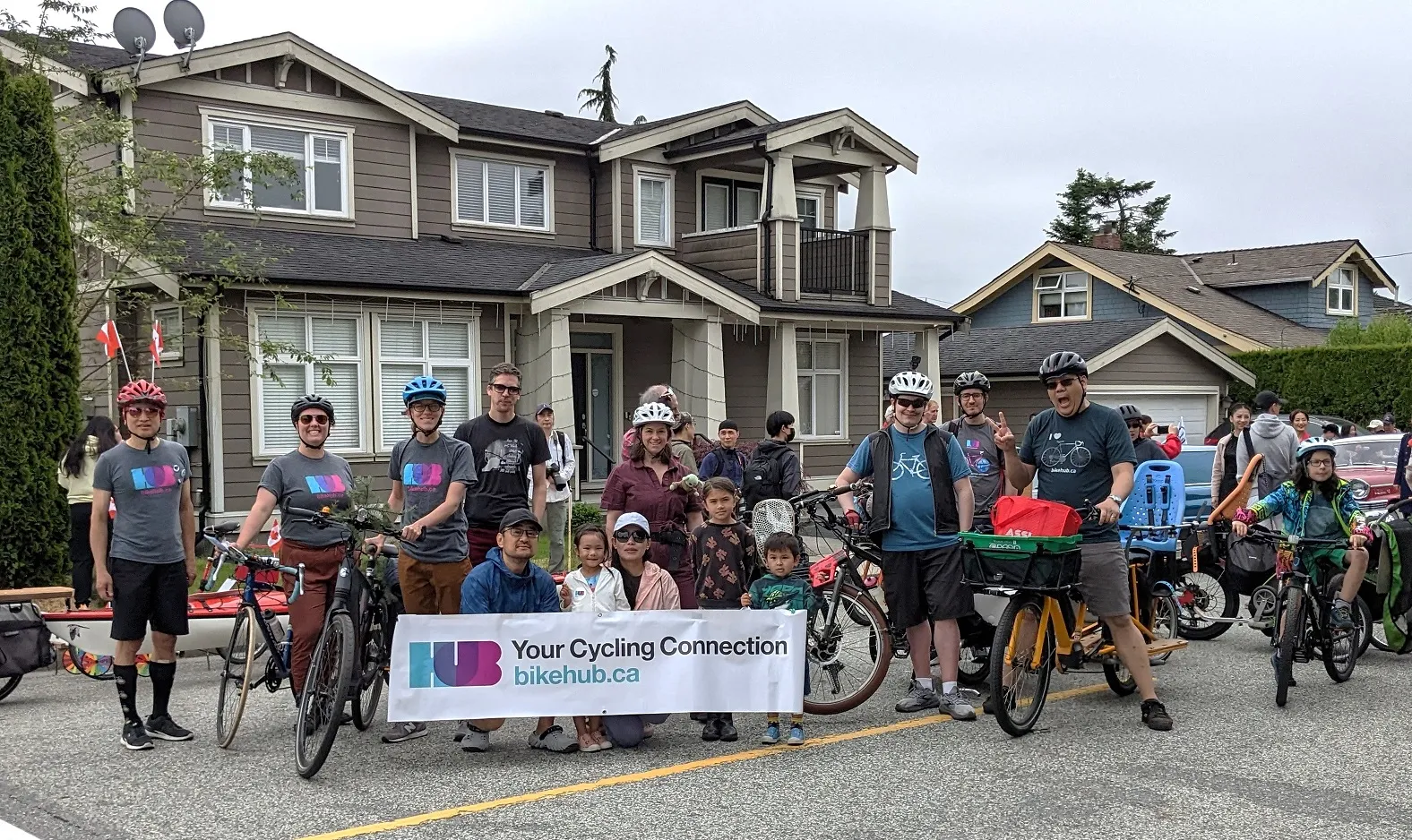 A group of New West cyclists pose for a photo with their bikes. They hold up a HUB Your Cycling Connection banner.