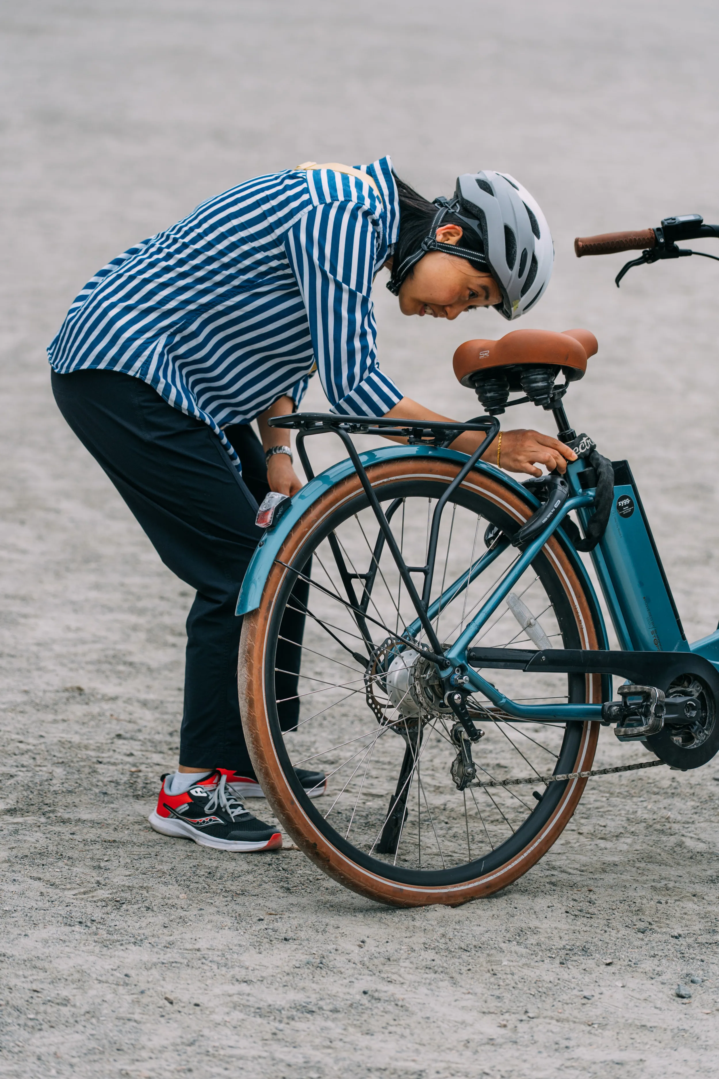 A woman bends down to inspect the back wheel of her bike.