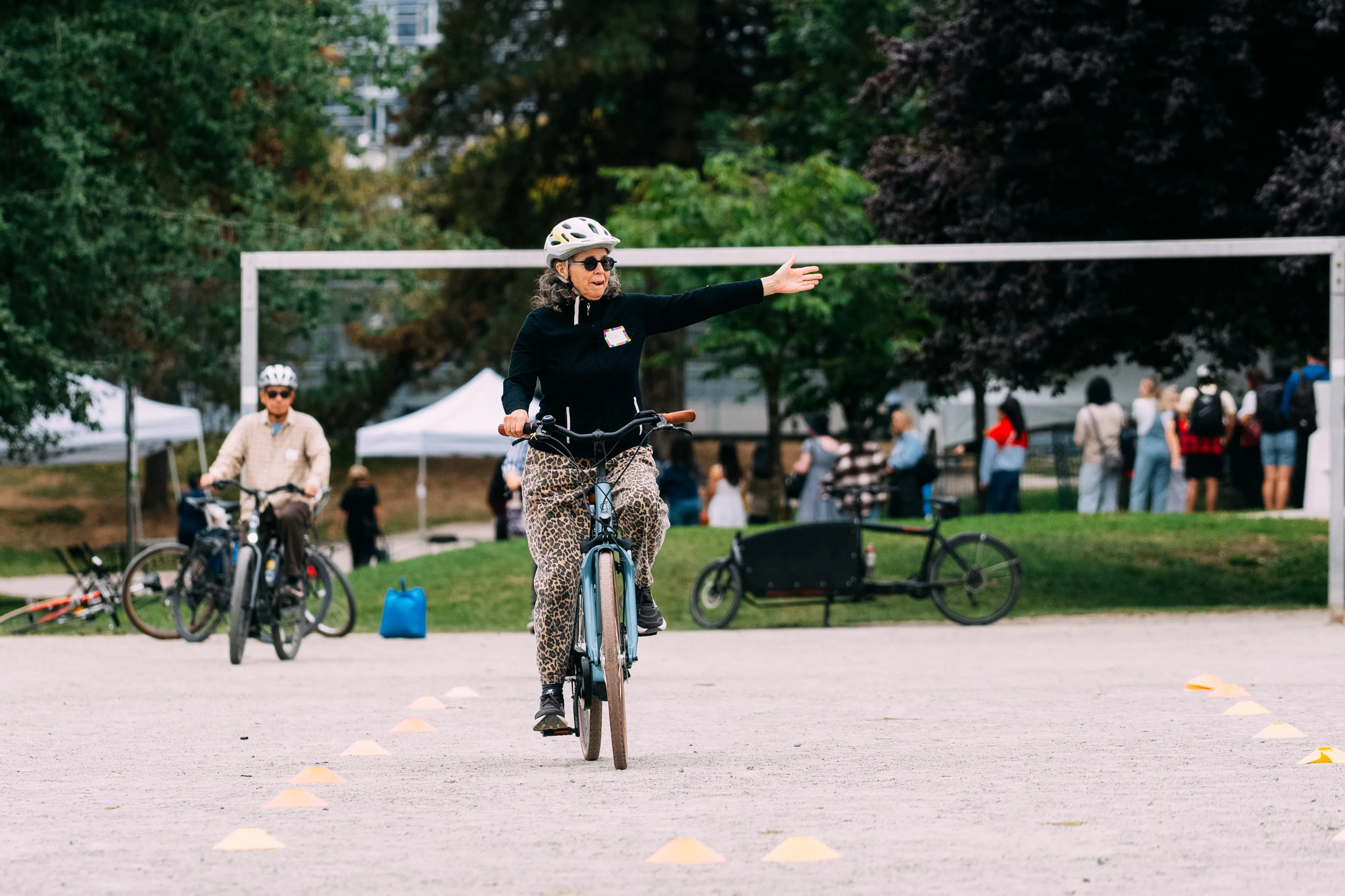A woman rides her bike on a gravel field and indicates a left turn signal.