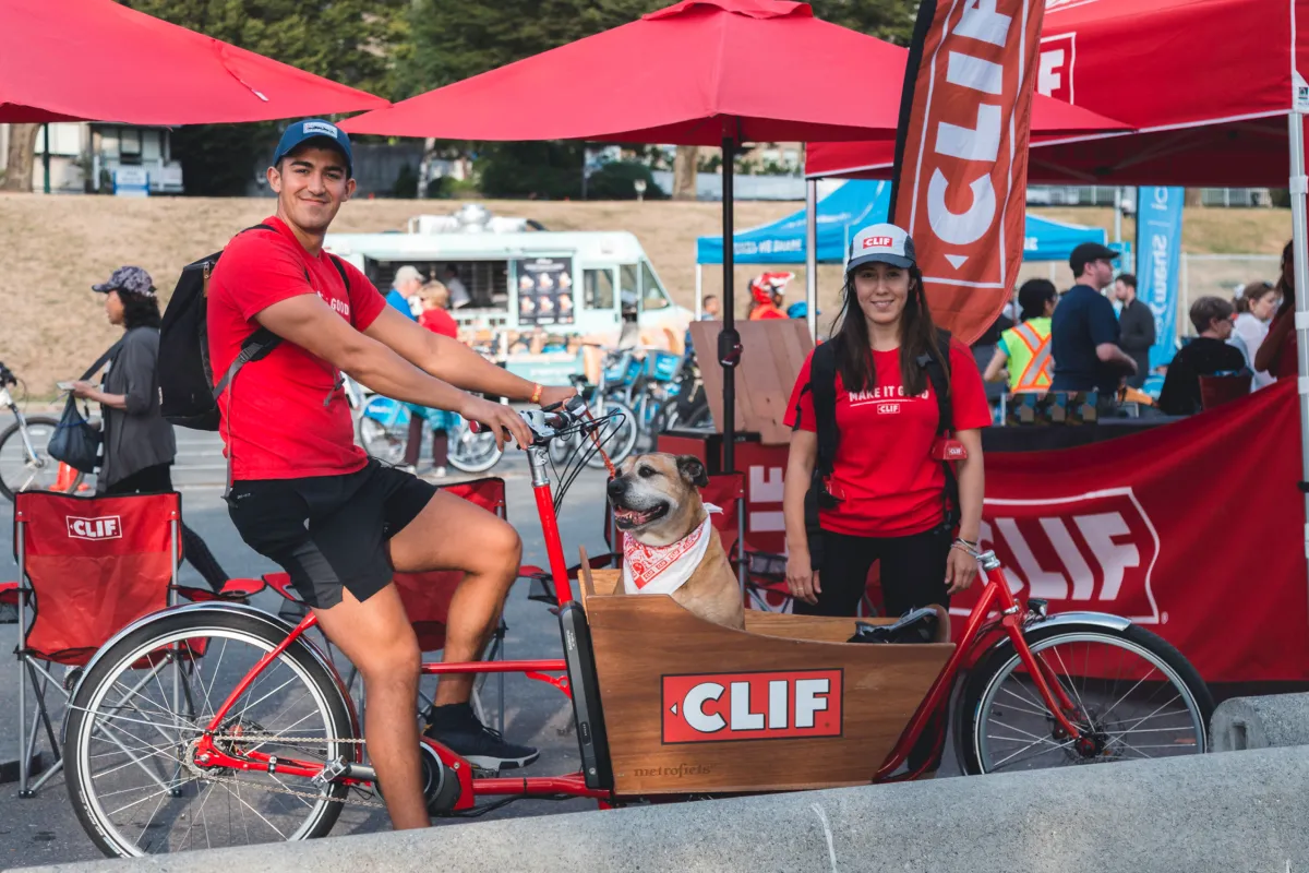 A young man and young woman stand with a CLIF branded cargo bike.