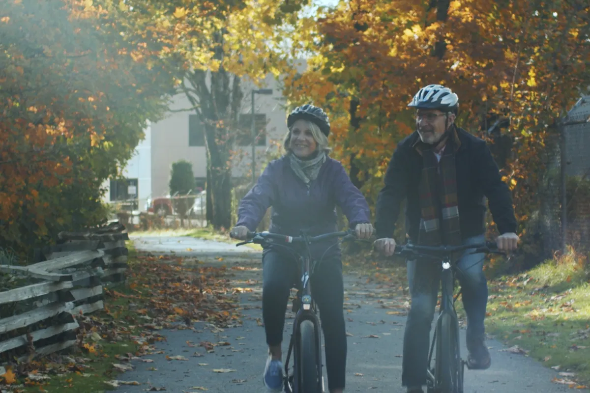 A senior couple rides bikes on a gravel path.