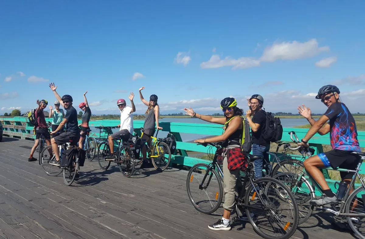 A group of people with their bikes wave on a bridge.