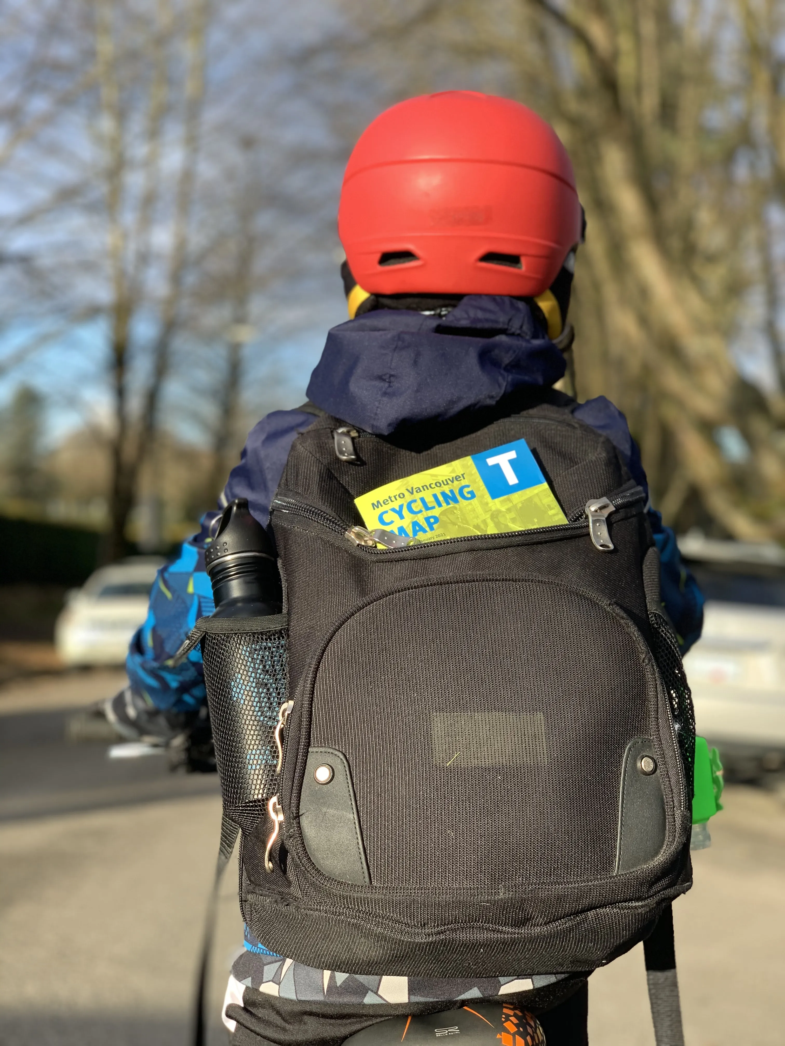 A boy rides his bike with a bike map sticking out of his backpack.