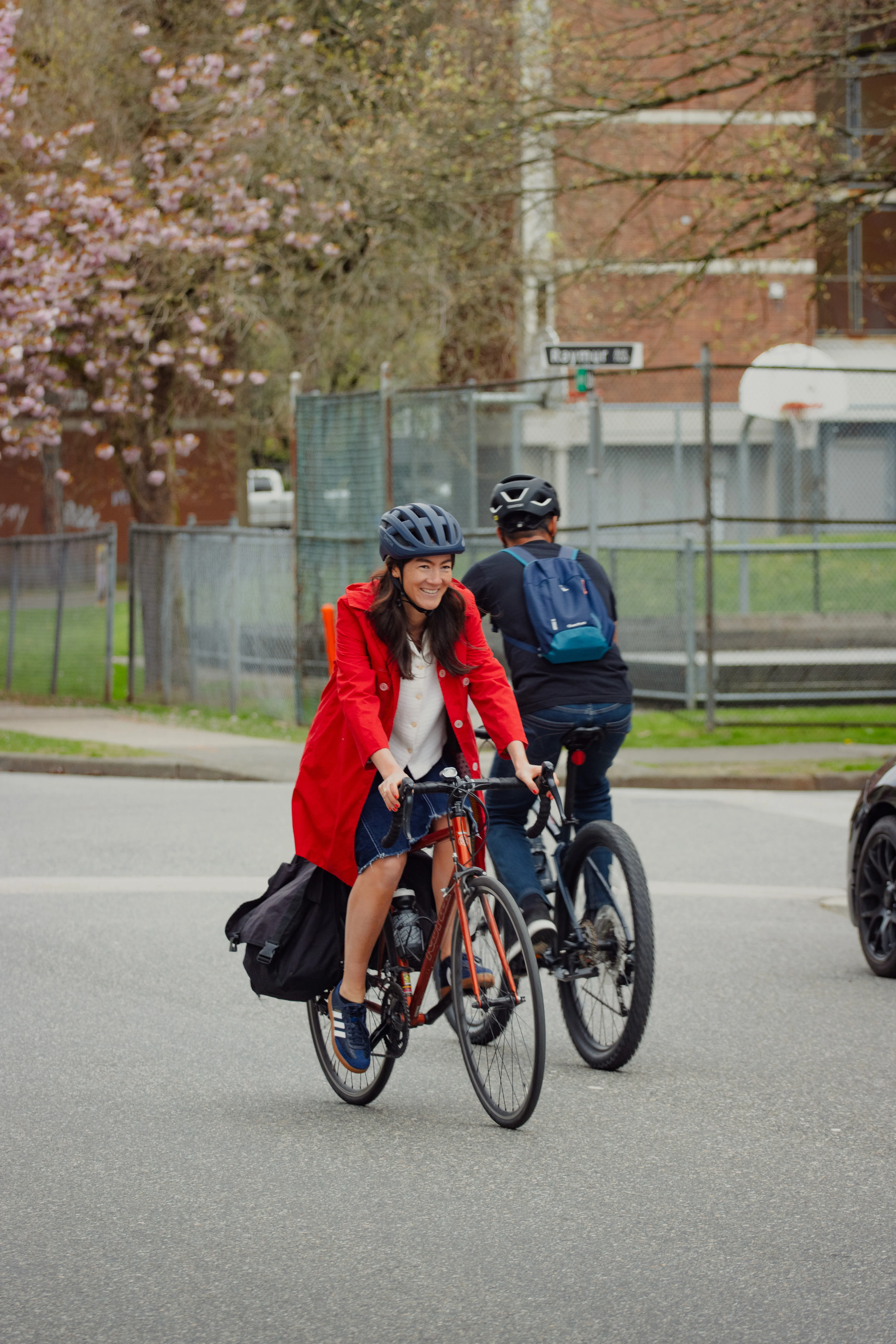 A woman in a red jacket rides a bike on a road. A man is riding a bike in the opposite direction.