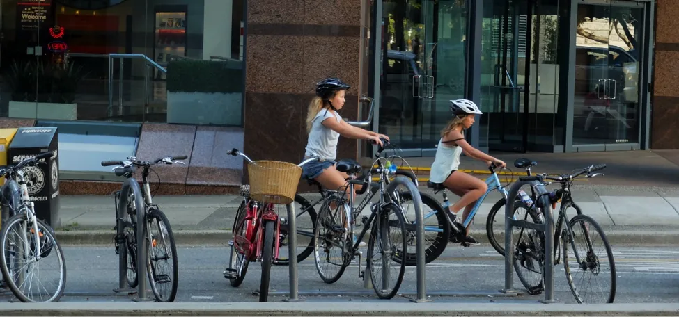 Two young girls ride bikes on a bike path in downtown Vancouver.