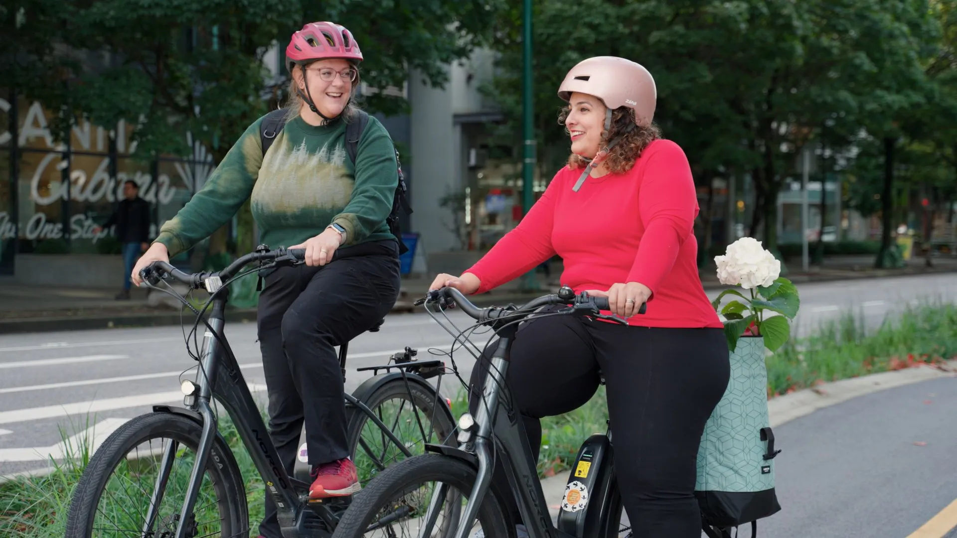 Two women ride bikes on a bike path. They are smiling and laughing.