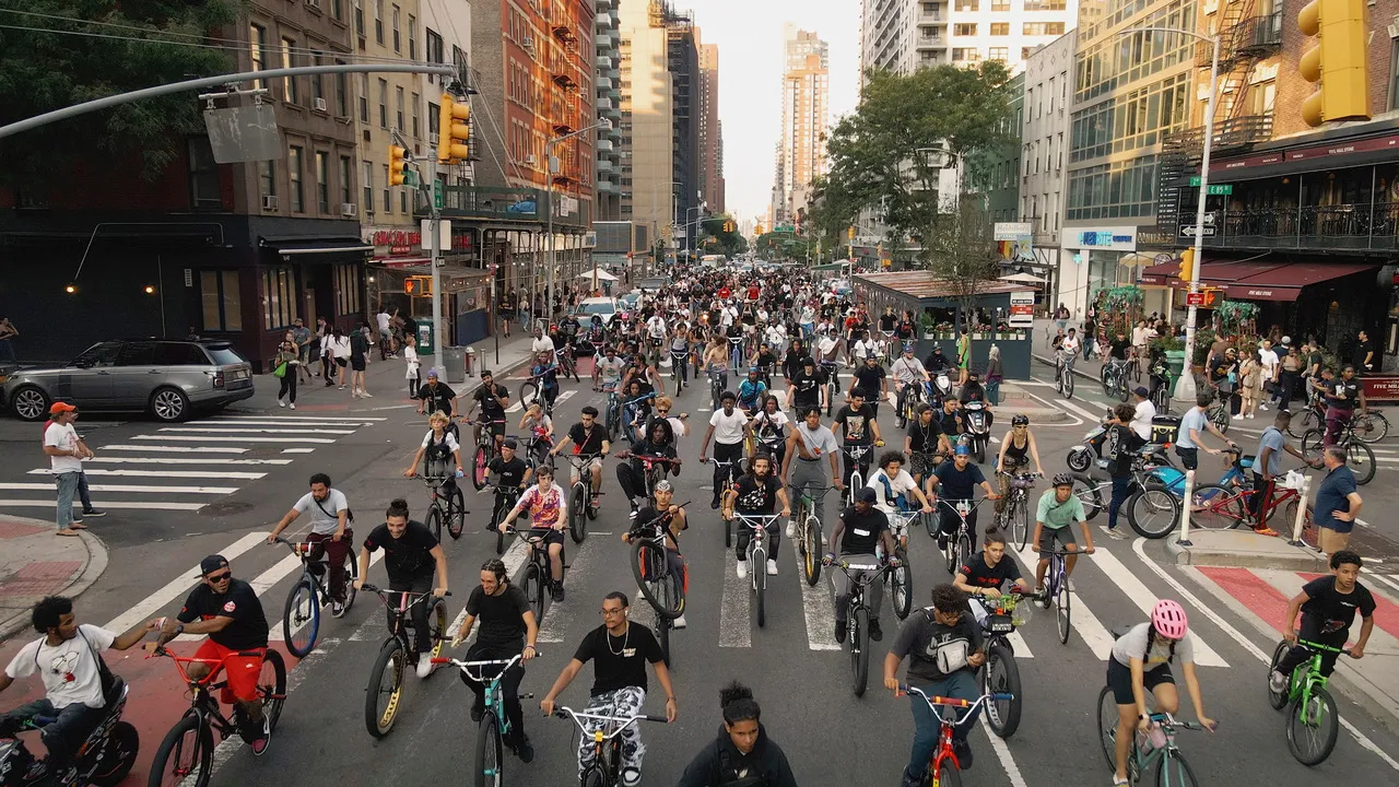 A group of people ride their bikes in mass down a city street.