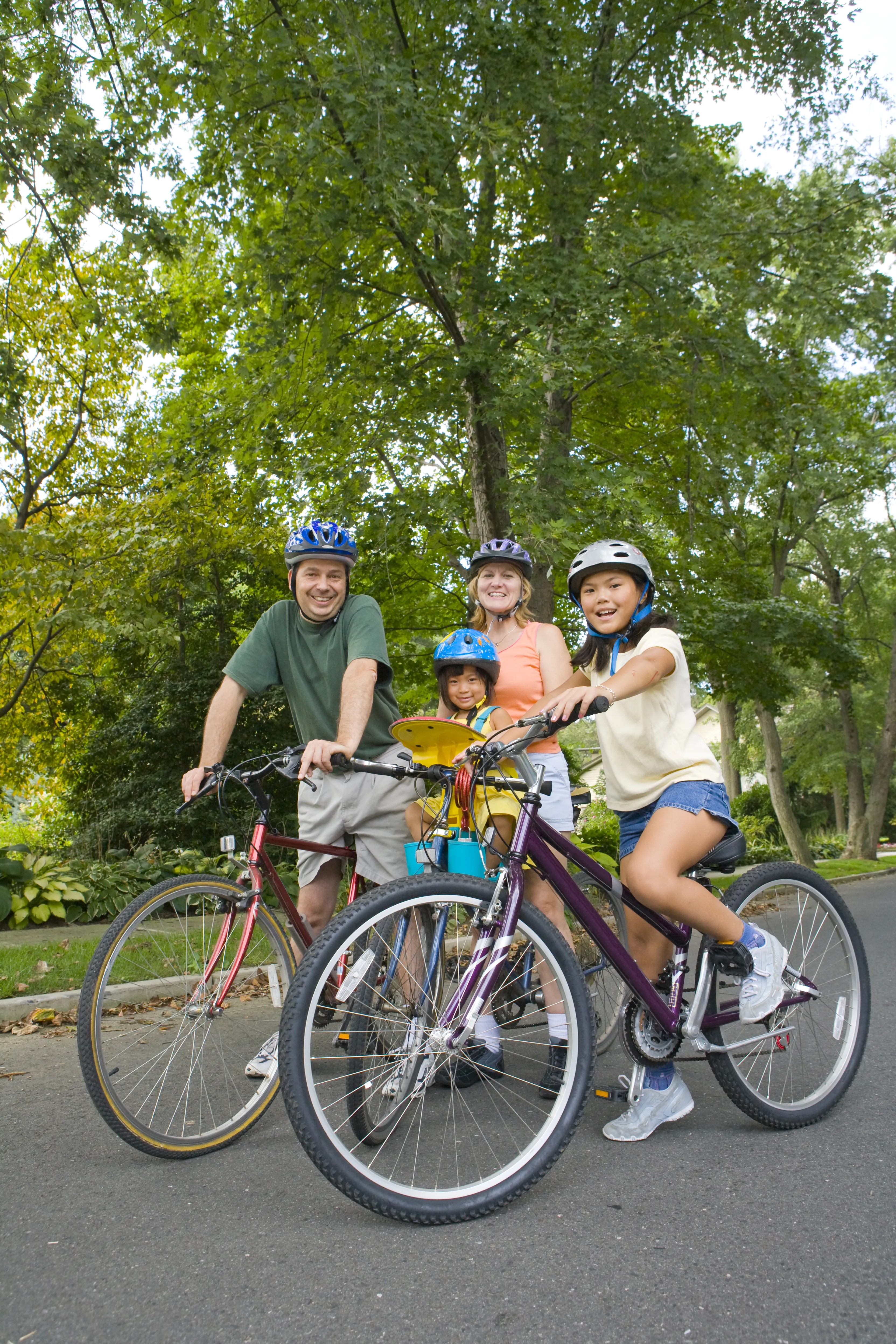 A family, parents with two kids posing with their bikes in a park